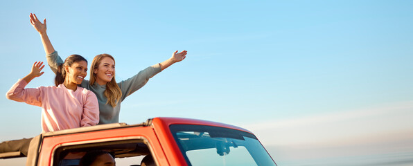 Couple With Friends On Vacation Driving Car On Road Trip Adventure To Beach Standing Up Through Roof