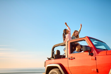 Couple With Friends On Vacation Driving Car On Road Trip Adventure To Beach Standing Up Through Roof