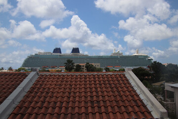 Cruise liner over the roofs of the Bonairian houses against blue sky with white clouds, Bonaire, Caribbean Netherlands - 774096292