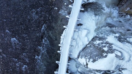Aerial top view of a bridge covered in snow and sea water nearby on a cold winter day