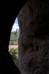 Vertical view out of a cave with green hills in the background on a sunny day