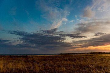 Sunrise or sunset in the Russian steppe at golden hour. Stratus, Cirrocumulus and Altocumulus clouds. The sun is shining from behind a cloud. Red orange and white shades. Morning or evening. - obrazy, fototapety, plakaty