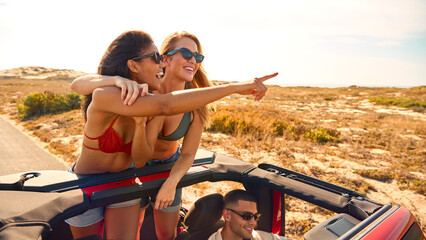Couple With Friends On Vacation Driving Car On Road Trip Adventure To Beach With Women Standing