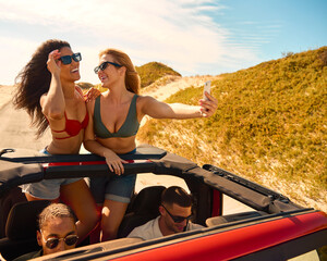 Couple With Friends On Vacation In Car On Road Trip To Beach With Women Standing Posing For Selfie