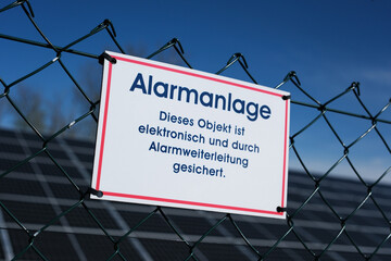Hinweis auf Alarmanlage am Zaun einer Solaranlage, Deutschland