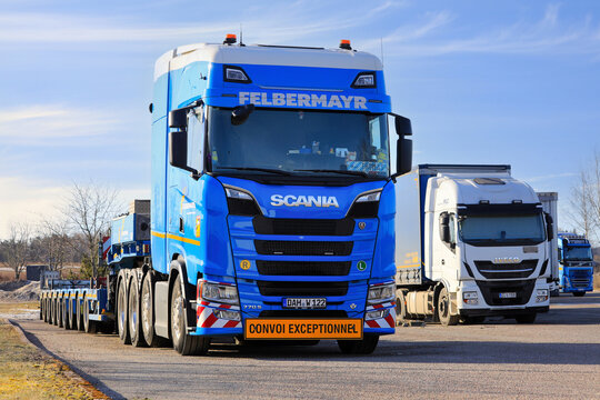 New blue Scania 770S truck in front of multi-axled heavy haul trailer parked on truck stop yard. 