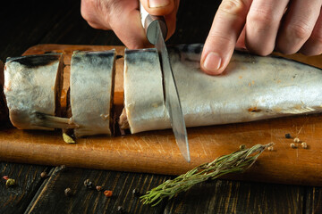 Close-up of a chef hands with a knife slicing mackerel before cooking. Low key concept for fish menu with spices and rosemary