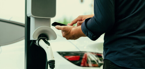 Man using smartphone online banking application to pay for electric car battery charging from EV...