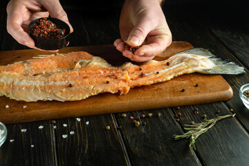 Cooking fish steak before grilling. The chef hand adds dry aromatic spices to fatty raw fish.