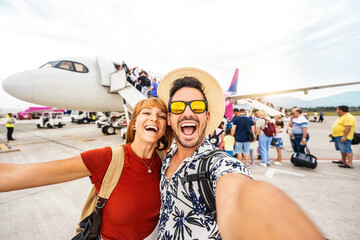 Happy couple of tourists boarding on a plane at the airport - Happy man and woman having happy summer vacation together - Transportation and holidays concept - obrazy, fototapety, plakaty
