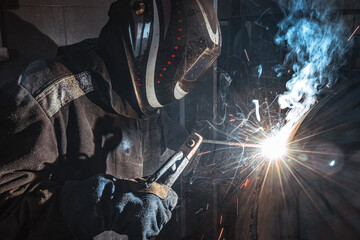 A welder diligently works in a factory, sparks flying as they expertly weld metal, showcasing skill...