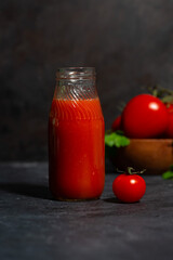 fresh tomato juice in a glass bottle on a dark background, vertical closeup