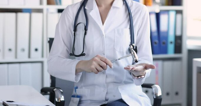 Neurologist knocks on palm with hammer at clinic workplace. Doctor neurologist consultation concept
