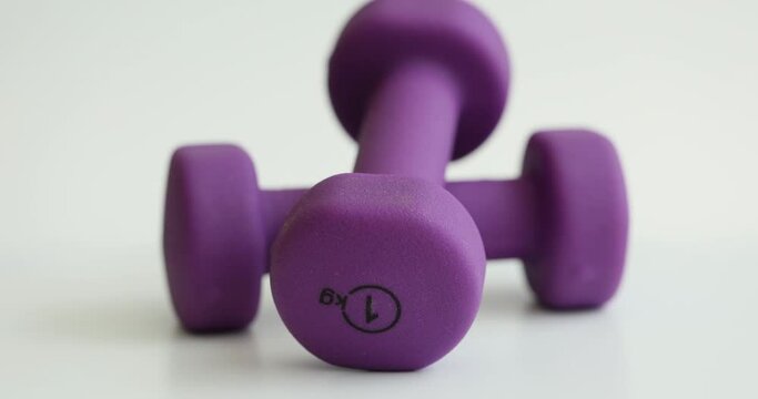 Purple dumbbells of 1 kg spinning on white background closeup 4k movie. Home female fitness concept