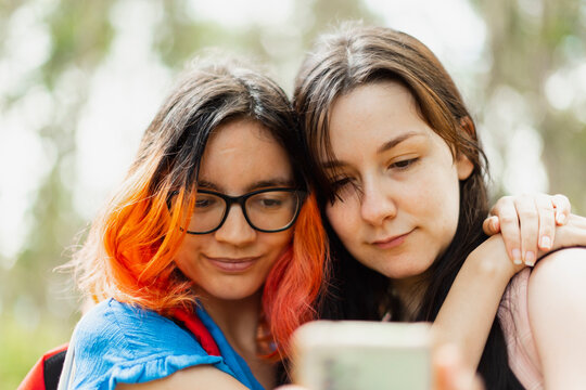 Two young girls hug each other while looking at the mobile phone to take a selfie