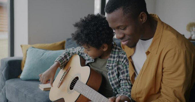 Adorable little child and adult man father playing the guitar together enjoying music and family life together. Happy childhood and fatherhood concept.