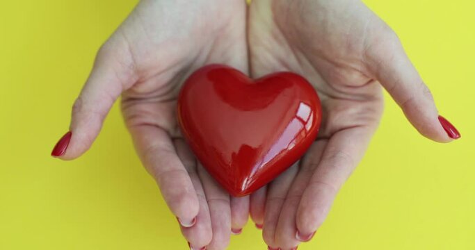 Female palms with heart opening on yellow background closeup 4k movie. Hope and charity concept