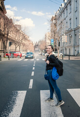 Beautiful smiling tourist woman with backpack standing on the crosswalk in the Belgrade city, Serbia