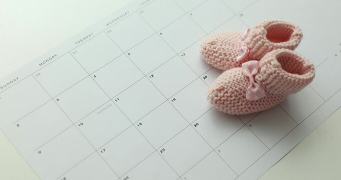 Baby pink booties for newborn on calendar closeup 4k movie. Pregnancy term childbirth concept