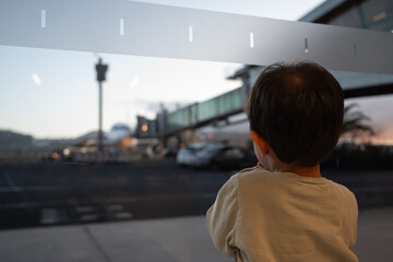 A young child is looking out a window at a busy airport. The scene is bustling with activity, with...