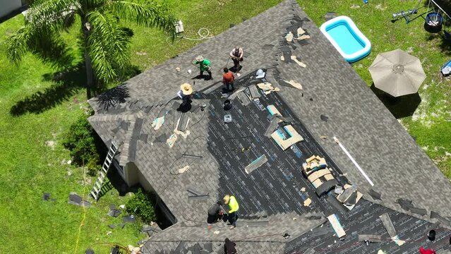 Construction workers installing asphalt shingles on residential private house roof. Rooftop covering on Florida home