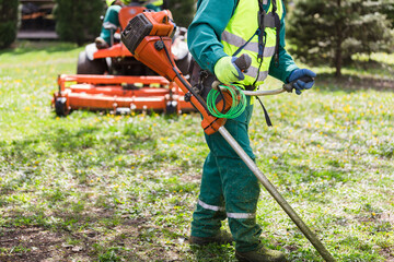 Worker using a weed trimmer in a park - 774161257