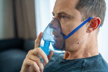 Unhealthy man wearing nebulizer mask in home. Health, medical equipment and people concept - obrazy, fototapety, plakaty