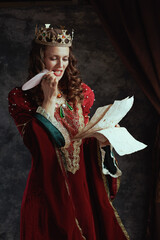 pensive medieval queen in red dress with parchment and crown