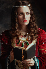 pensive medieval queen in red dress with book and rosary