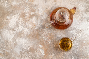 Red tea with herbs in glass teapot on brown concrete. Top view, copy space.