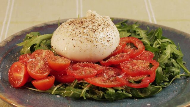 Burrata or Mozzarella cheese on fresh tomatoes and green arugula on plate close-up. From Italian cow's milk cheese made from mozzarella and cream.The outer casing is solid