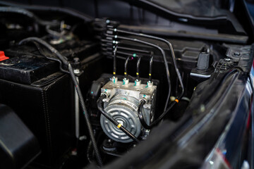A car engine is opened up and the hood is up. The engine is black and has a lot of wires and tubes