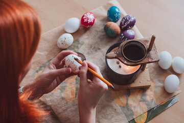 Woman hand painting easter egg with wax from candle. Traditional holiday habit, lifestyle background - 774173863