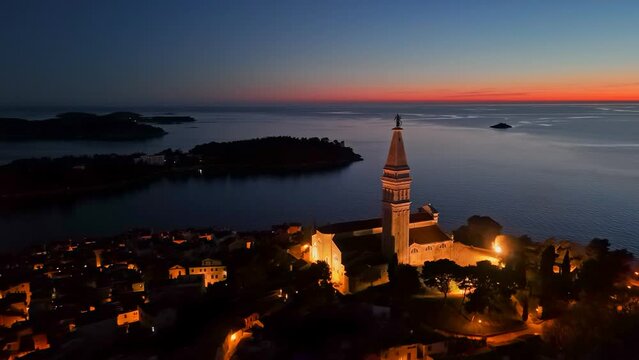Night shot of Church of Saint Euphemia in old town of Rovinj, Croatia. Sea and sunset sky at background, aerial shot, 4K