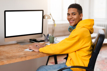 Smiling black teen guy at computer desk with blank screen