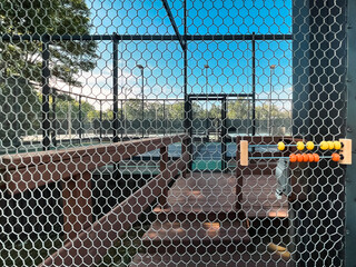 Summertime scene of elevated sport courts with nets in a public park setting. Courts are used for paddle tennis or pickleball play. Focus on wooden score counter affixed to the chicken wire fence.