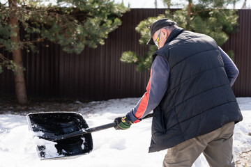 Seasonal work in the garden, a man clears snowdrifts in early spring to get to the tree. High...