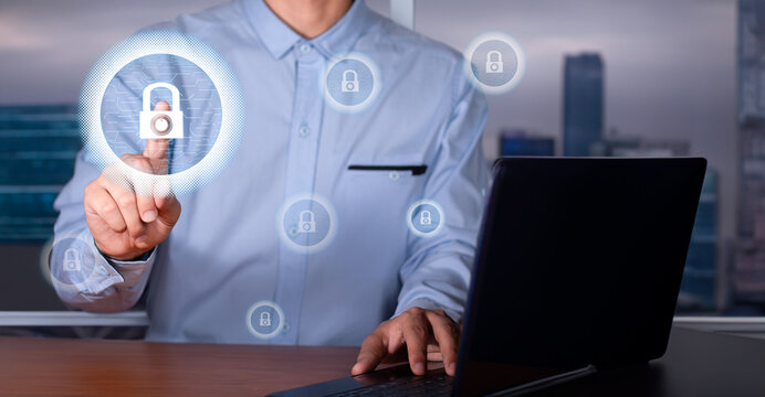 cybersecurity concept. executive in office in front of laptop touches padlock hologram on a circuit board.