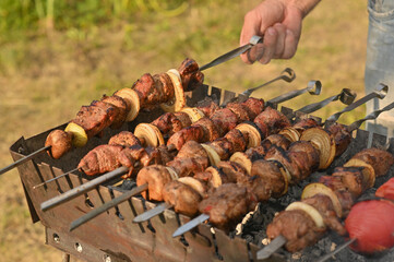 A man's hand turns over a skewer with meat on the grill.