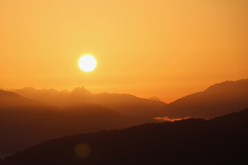 early morning sun rising over a hazy mountain range in an orange sky - Powered by Adobe