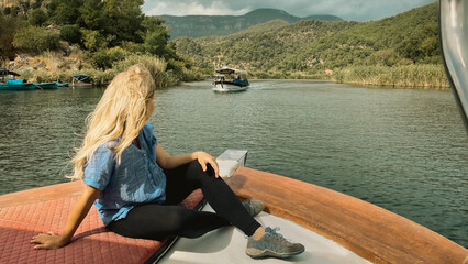 Girl sitting on boat and watching beautiful nature scene on Dalyan river. Mugla, Turkey.