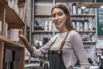 Young smiling female barista taking coffee sort at shop for customer. Close up portrait of...