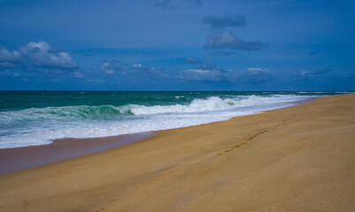 Tranquil scene of waves crashing on a sandy beach under a cloud-dotted sky