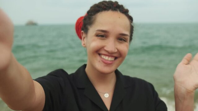Young caucasian pretty woman with red dreadlocks showing sign v, making selfie with happy smile with ocean beach on background