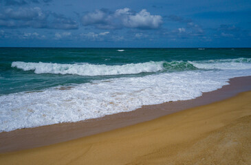 Tranquil scene of waves crashing on a sandy beach under a cloud-dotted sky