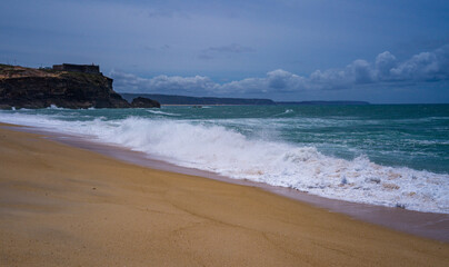 Tranquil scene of waves crashing on a sandy beach under a cloud-dotted sky