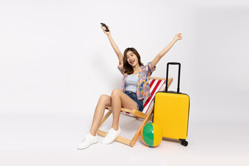 Happy Young Asian traveler woman wearing floral dress sitting on beach chair with yellow suitcase bag and holding mobile phone isolated on white background, Tourist concept - 774191256