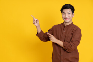 Young Asian man smiling and pointing to empty copy space isolated on yellow background