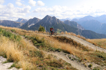 rider on a mountain bike, clad in protective gear riding on a mountain trail with a backdrop of high mountains