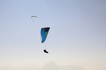  two paragliders in the air with a monochrome background of a hazy mountain range in different...